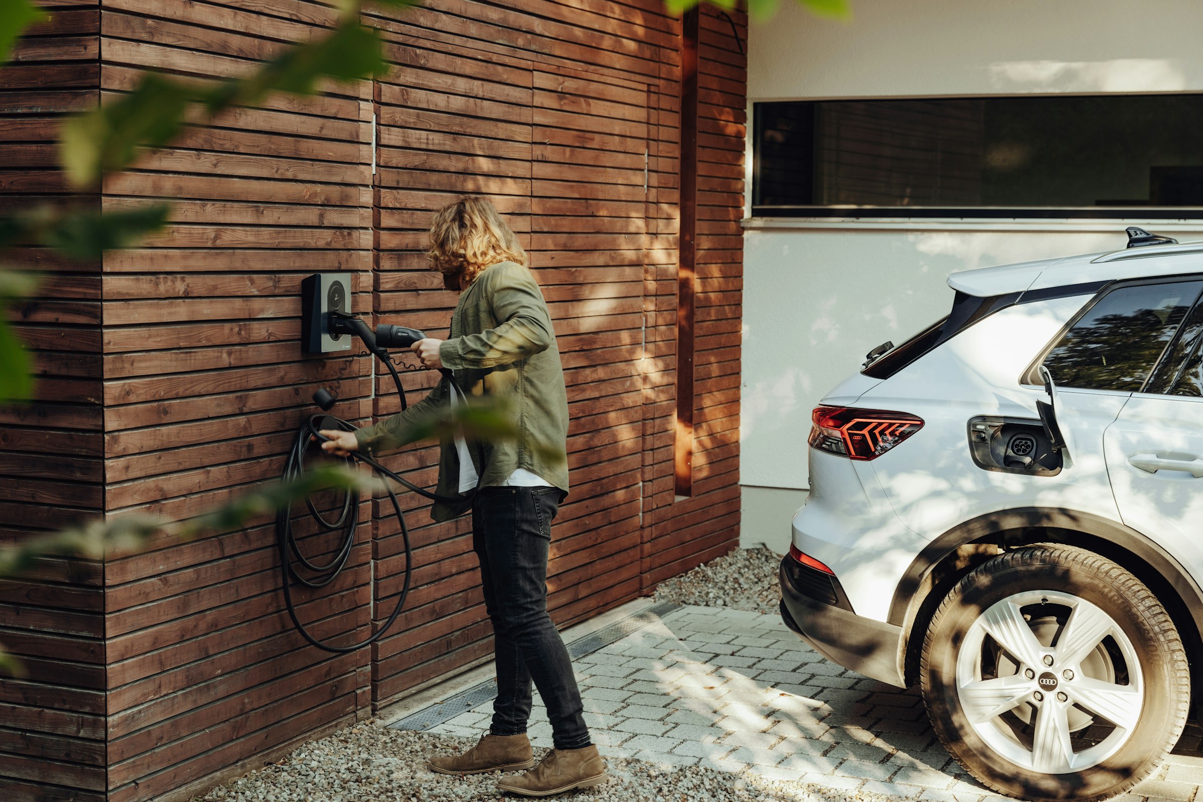 Man sluit de laadkabel van een thuislaadpaal aan bij een elektrische auto